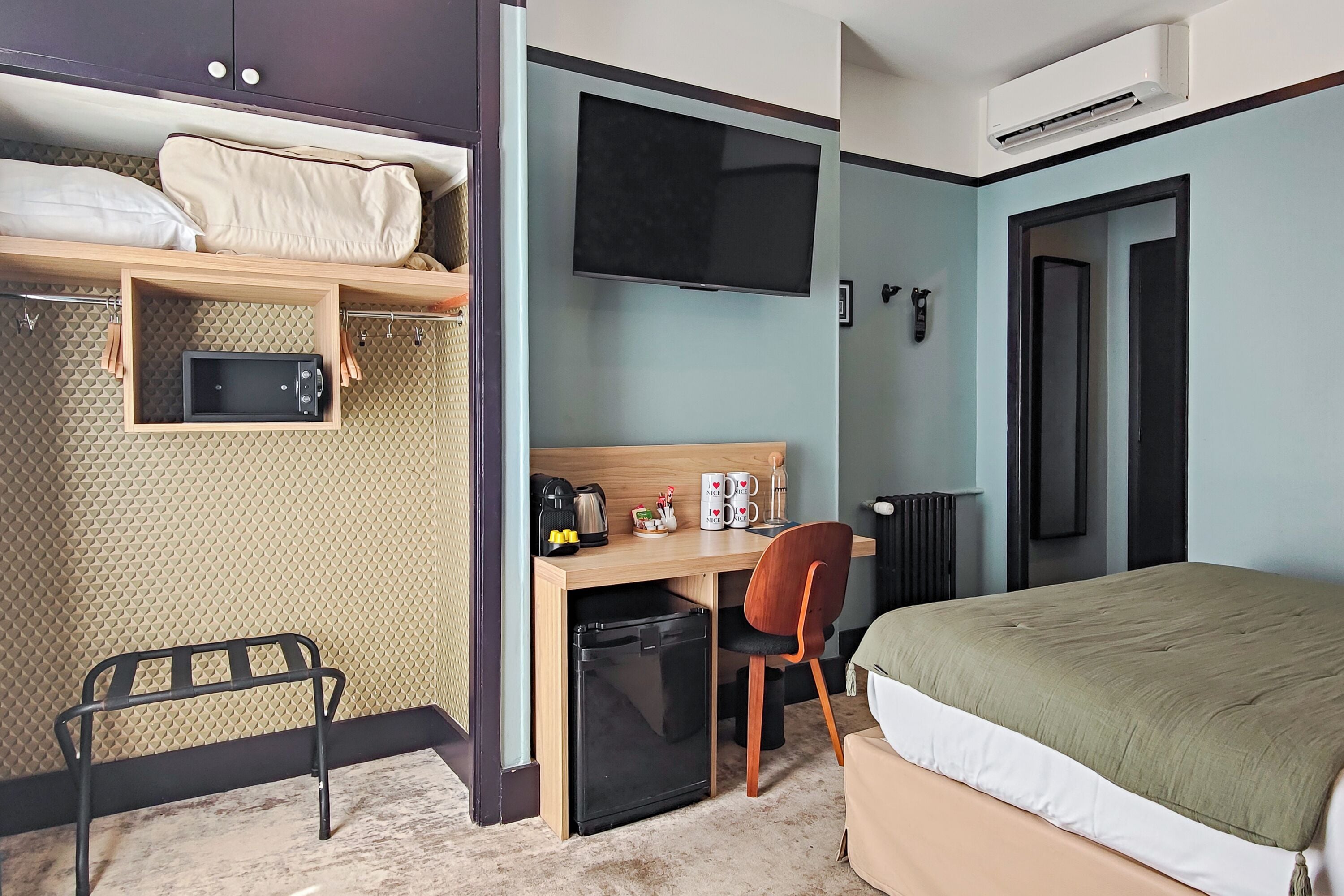 A compact hotel room with a bed, a desk with a chair, a TV, a microwave, and a small refrigerator.