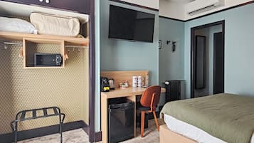 A compact hotel room with a bed, a desk with a chair, a TV, a microwave, and a small refrigerator.