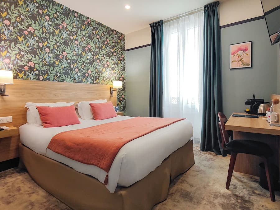 Una habitación de hotel con una cama grande, un escritorio con una silla, un televisor y un papel tapiz con motivos florales.