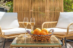 A wicker table with a glass top, two wicker chairs with white cushions, a wicker basket with oranges and apples, and two glasses of champagne. - Hôtel de France, un hôtel AMMI (Nice)