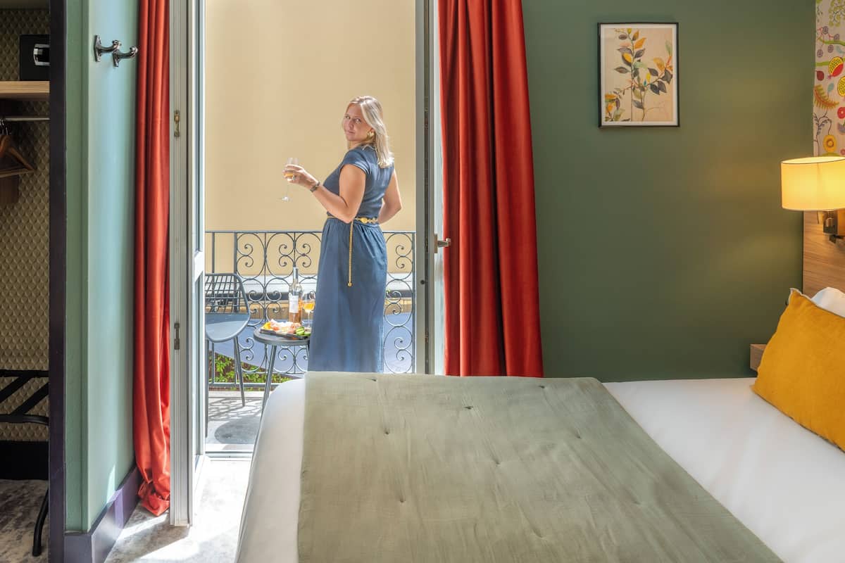 Ein Hotelzimmer mit Bett, Essecke mit Tisch und Stühlen sowie ein Balkon mit roten Vorhängen.