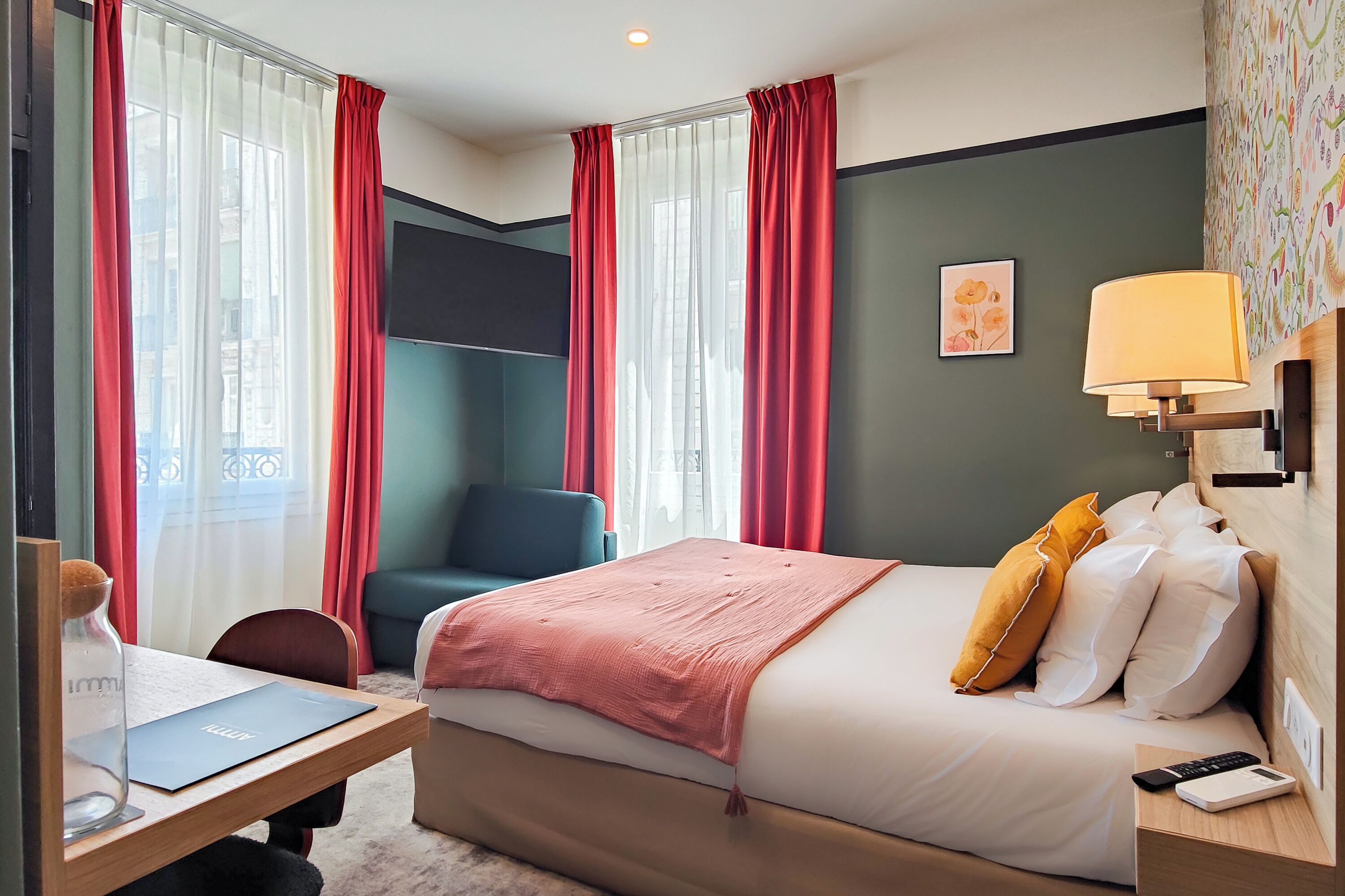 Ett hotellrum med en säng, ett skrivbord, en stol, en lampa och ett fönster med gardiner.