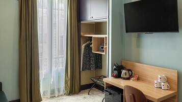 A hotel room with a bed, a desk with a chair, a TV, a wardrobe, and a window with curtains.