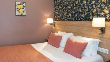 A neatly made bed with white and orange pillows, a wooden headboard, and two wall-mounted lamps.