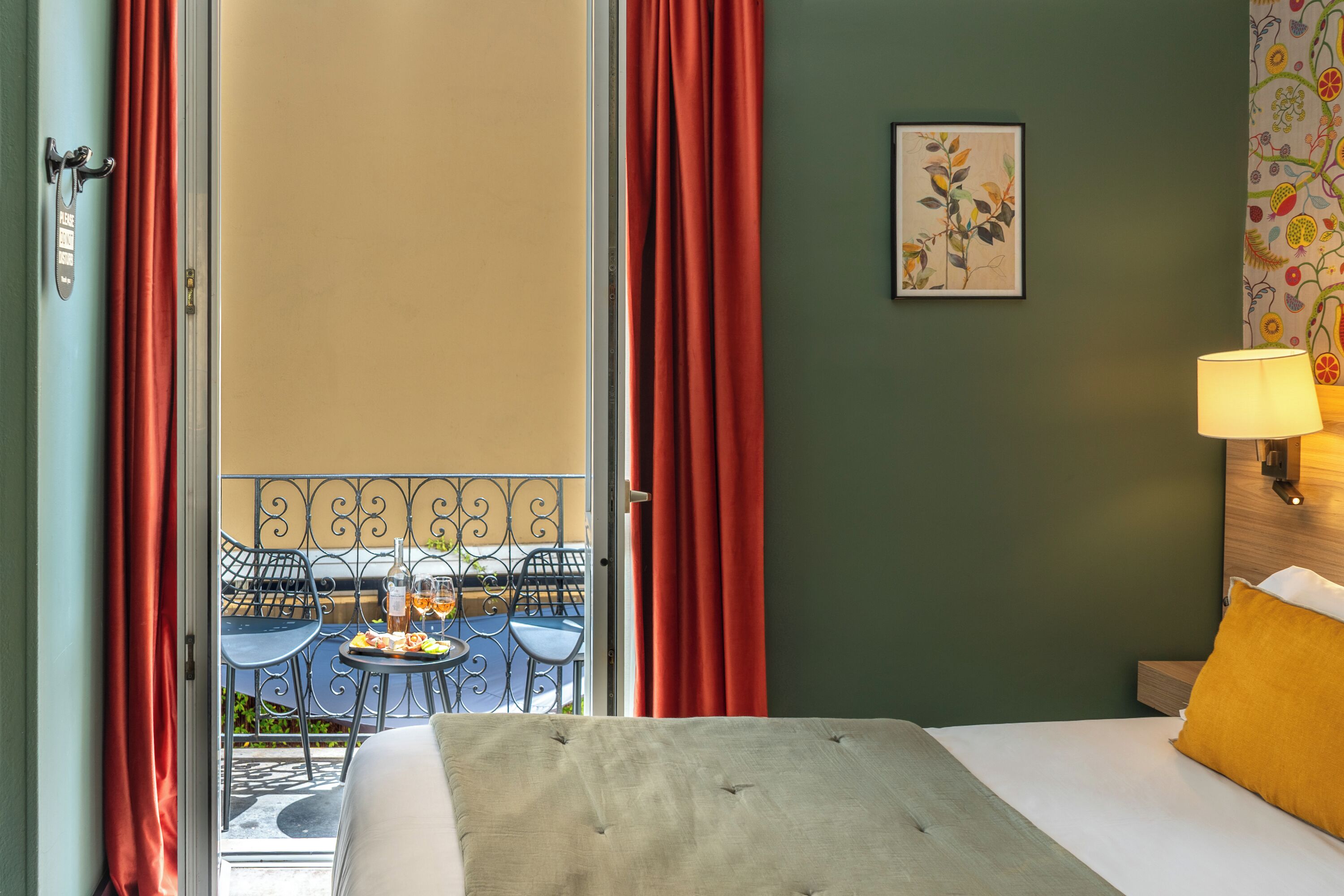 Ein Hotelzimmer mit Bett, Nachttisch, Lampe, einem Balkon mit Tisch und Stühlen sowie Blick ins Freie.