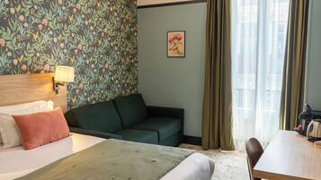 Una habitación de hotel con una cama, un sofá verde, una mesa de madera y una ventana con cortinas.