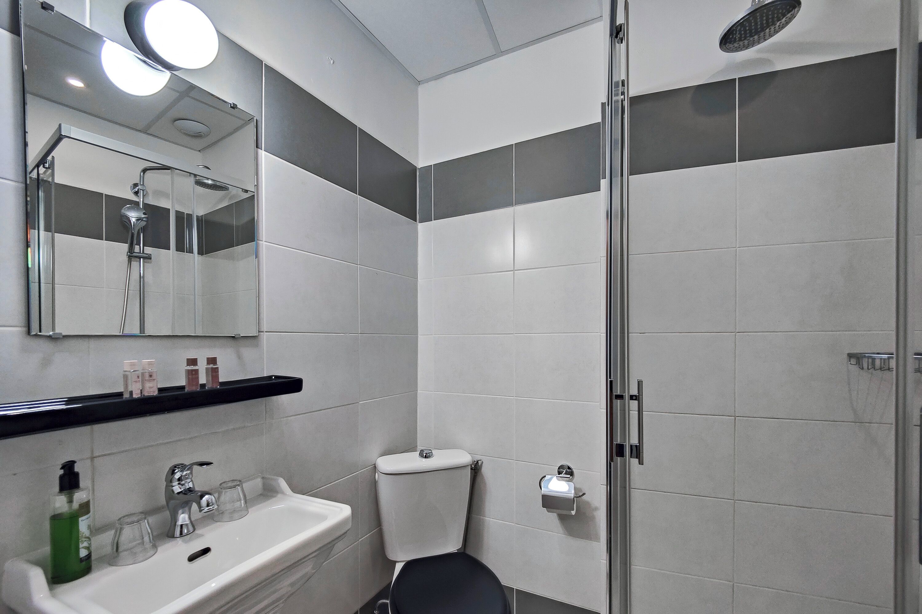 A modern bathroom with a glass shower enclosure, a white sink with a mirror above it, and a toilet with a paper towel dispenser.