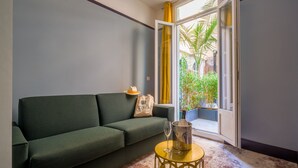 A room with a green sofa, a small round table with a glass, and a bag on the sofa. - Hôtel de France, un hôtel AMMI (Nice)