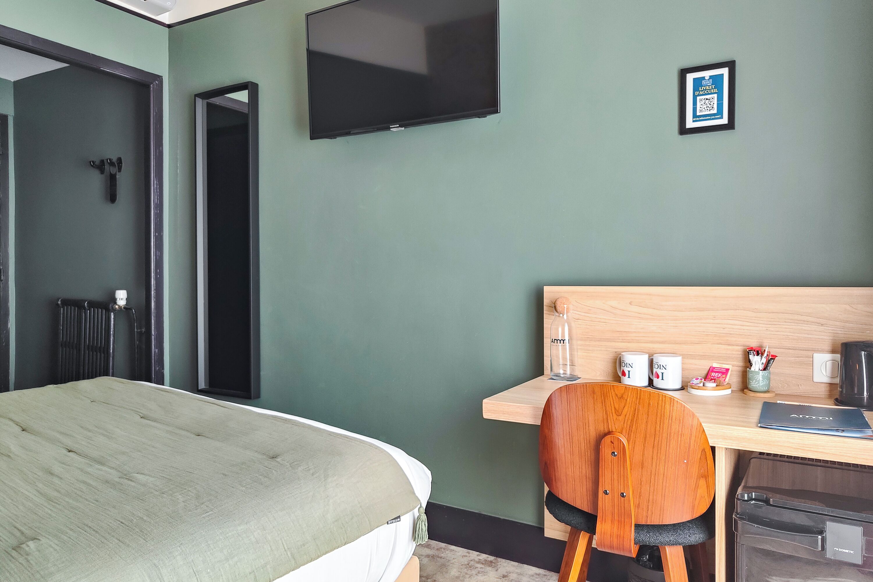 A hotel room with a bed, a desk, a chair, a television, and a framed sign on the wall.