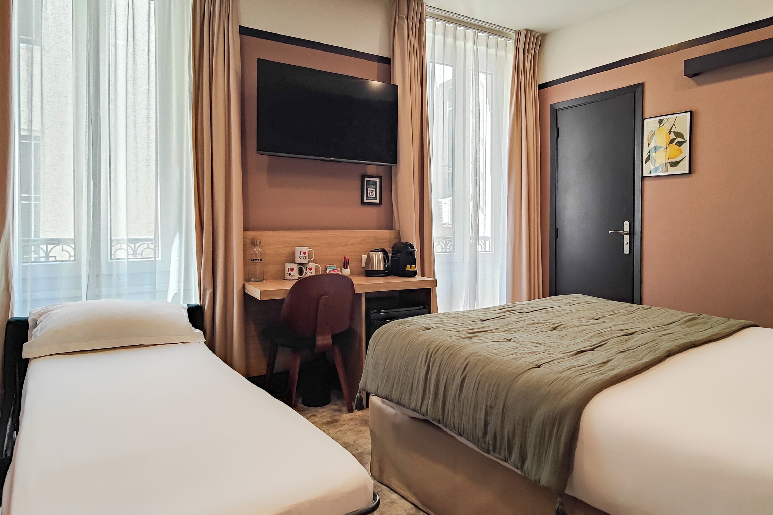 A hotel room with two beds, a desk with a chair, a television, and a door.