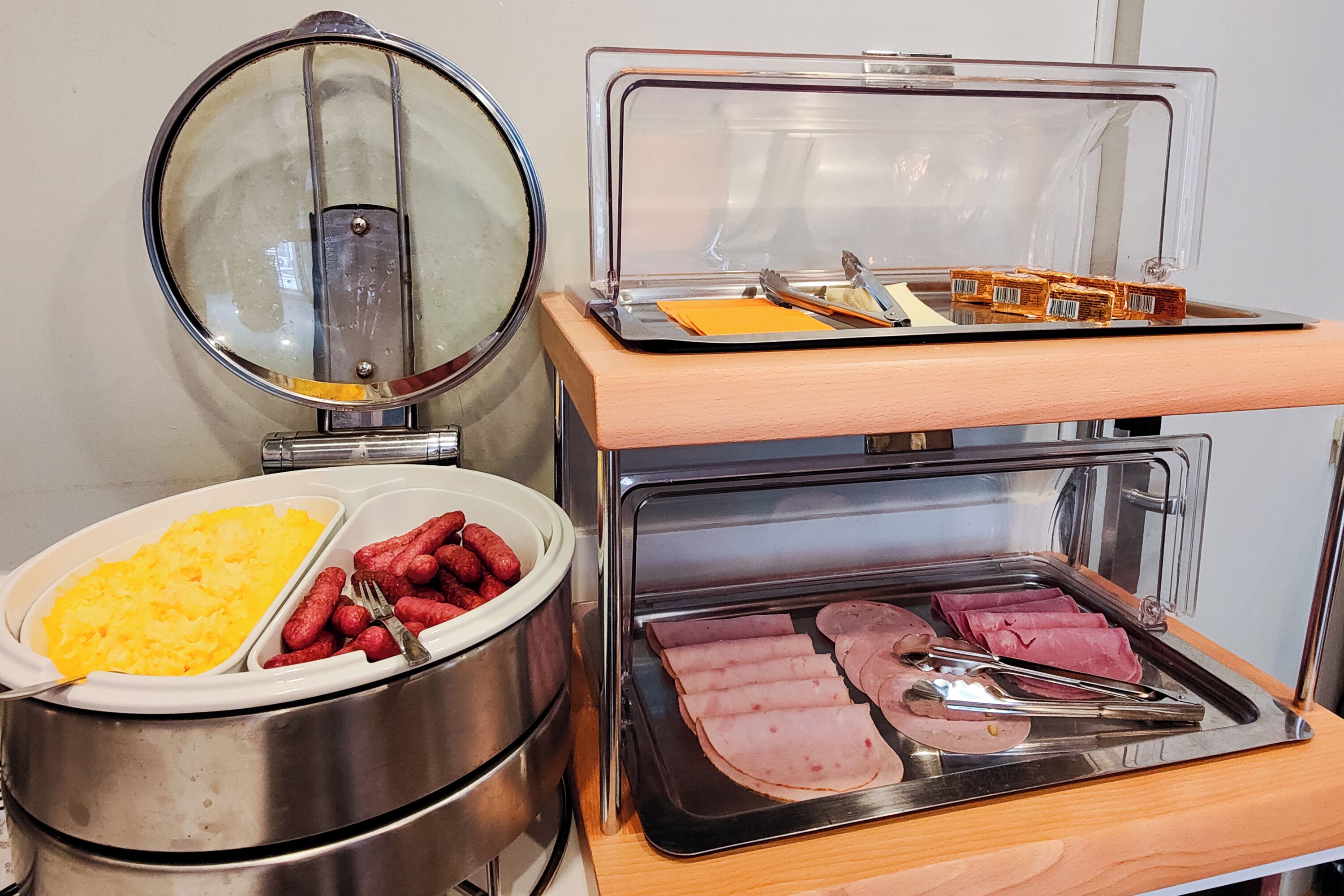 Montaje de bufé con diversos alimentos, como salchichas, jamón y huevos revueltos.