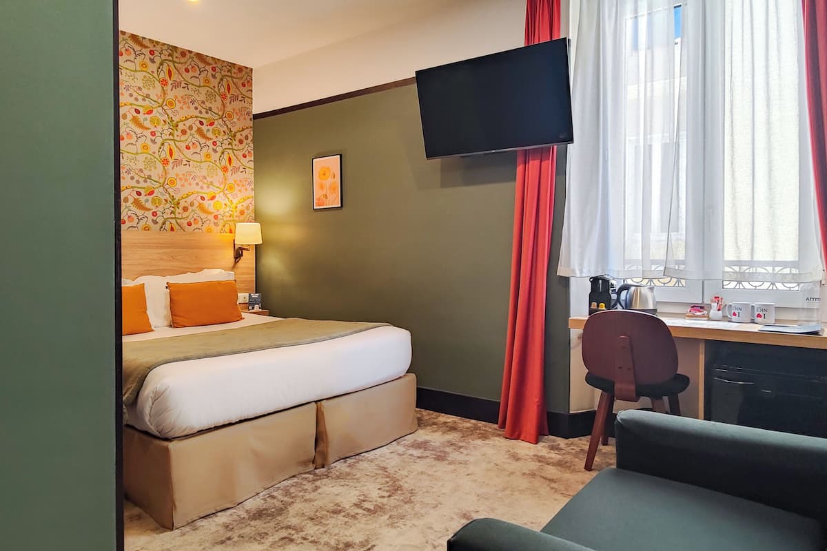 Ein Hotelzimmer mit Bett, Schreibtisch, Stuhl, Fernseher und einem Fenster mit Vorhängen.