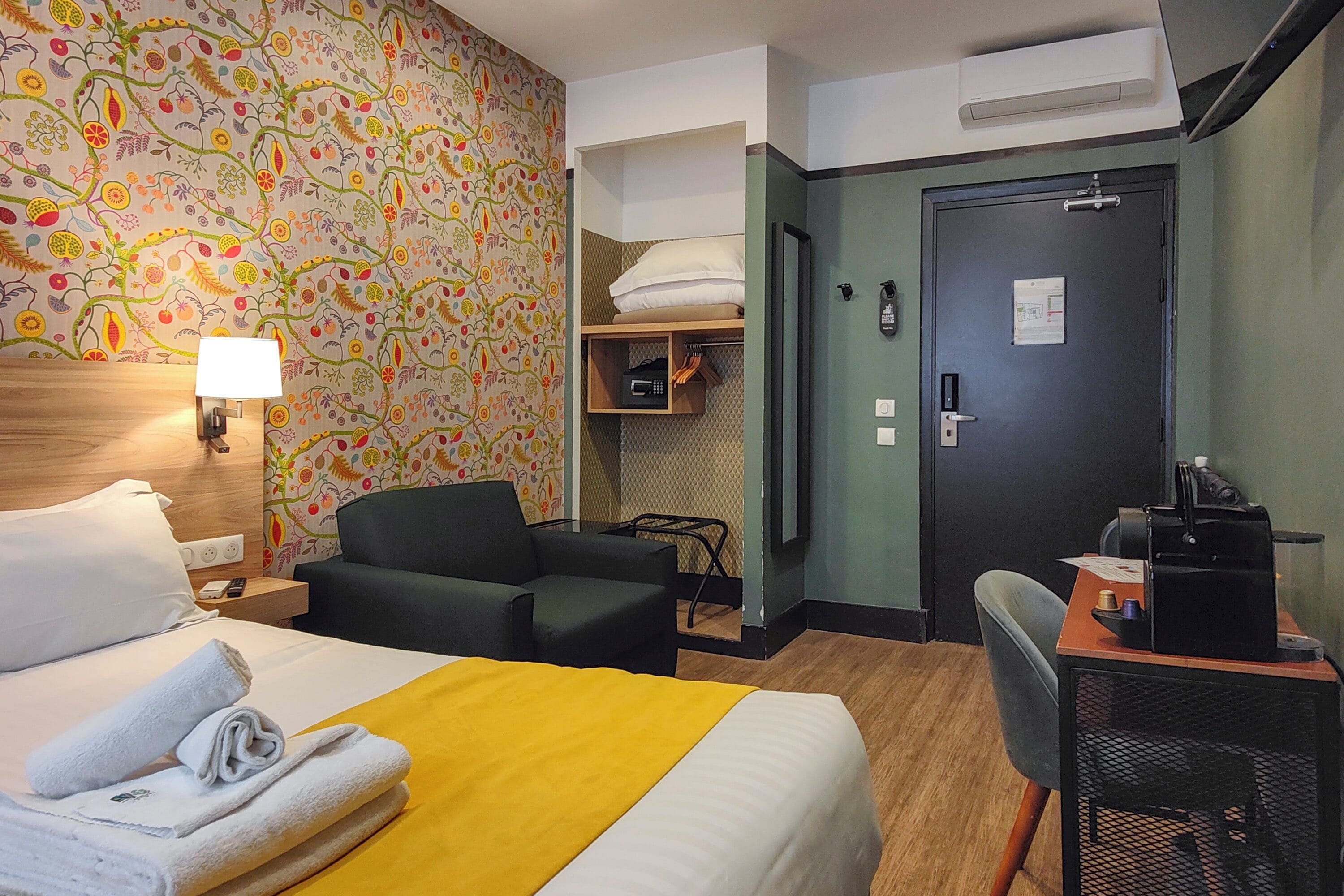 Een hotelkamer met een bed, een bureau met stoel, een bank, een kledingkast en een deur met slot.