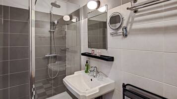Un baño moderno con ducha de vidrio, un lavamanos blanco, un espejo y un toallero negro.