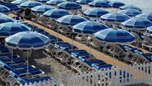 A beach with rows of blue umbrellas and white lounge chairs, a white picket fence, and a clear view of the sea. - Villa Rivoli (Nice)