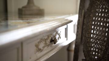 A close-up of a white dresser with a drawer handle, a decorative metal piece, and a lace curtain.