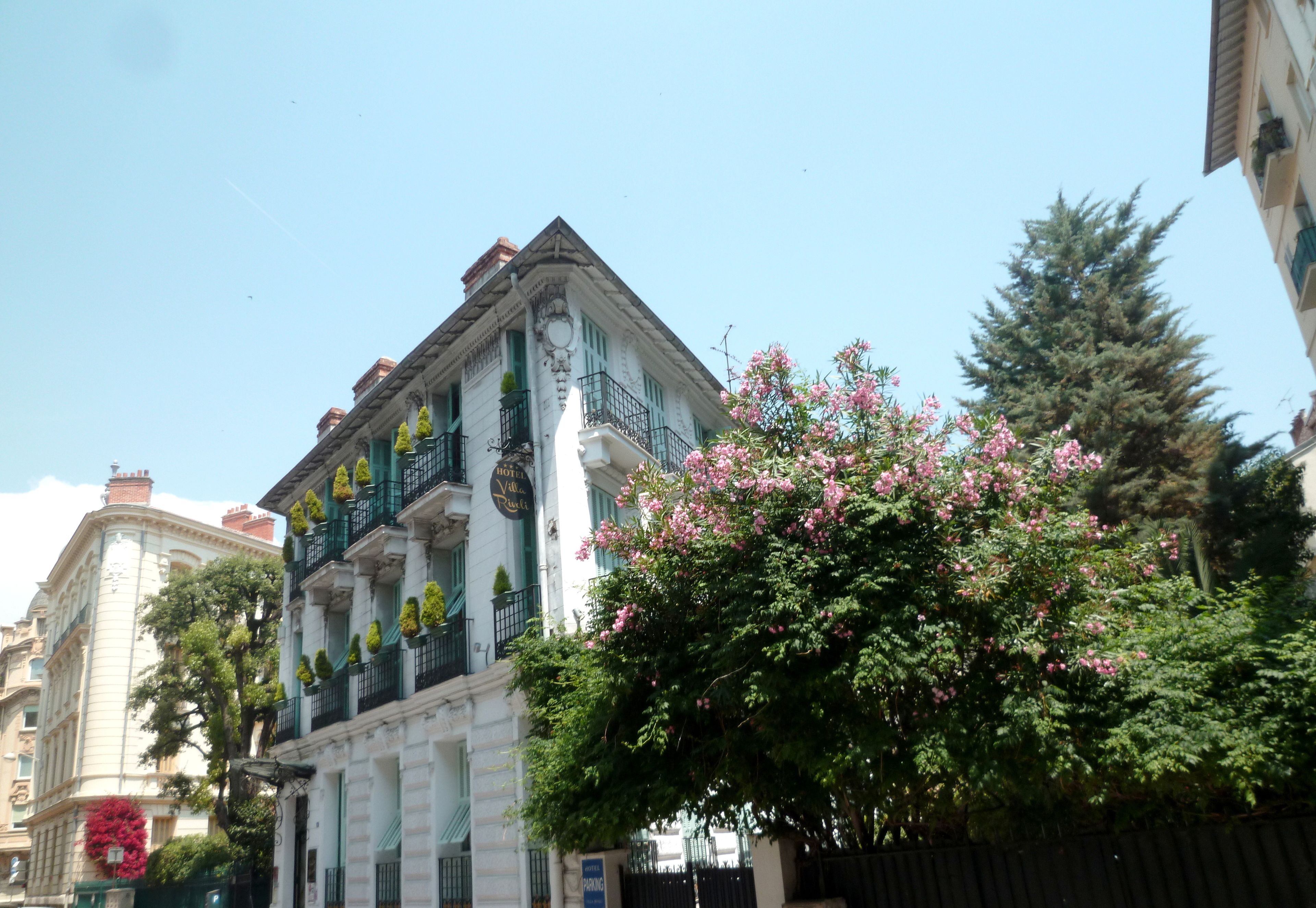 A historic building with a classic architectural style, featuring a prominent balcony with green railings and a sign indicating it is a hotel.