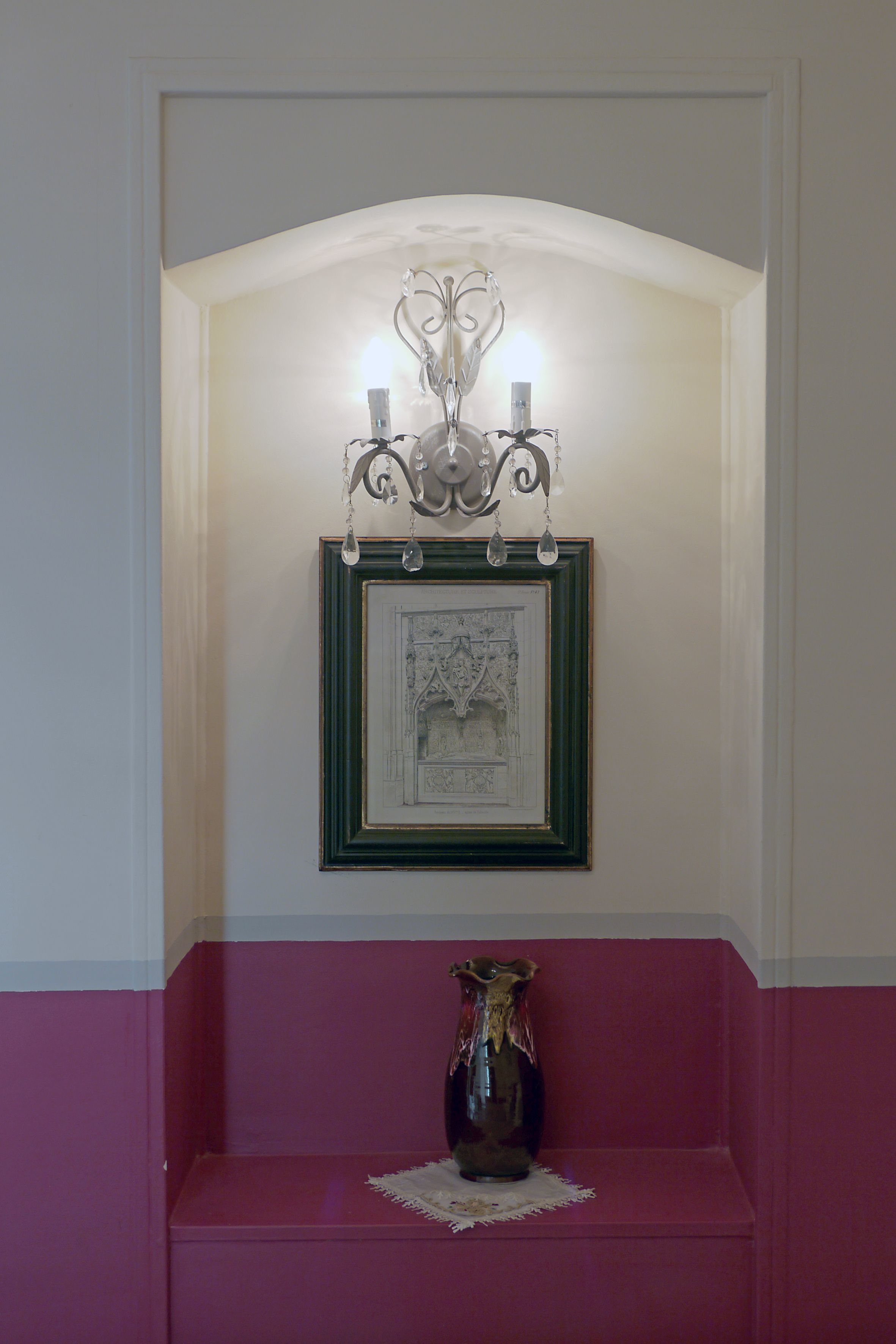 A framed architectural drawing on a wall, a vase on a shelf, and a wall-mounted light fixture.