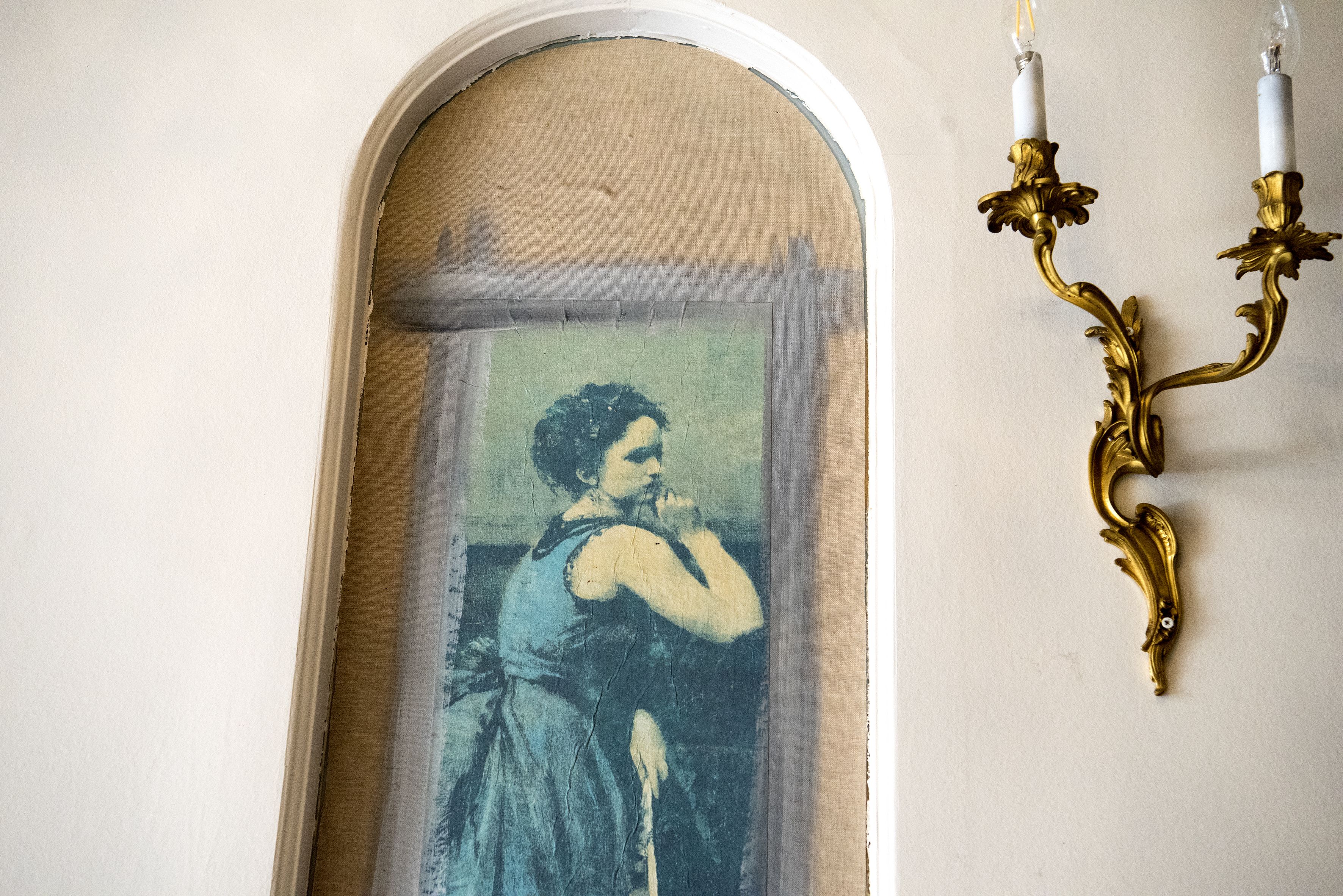 A room with a partially visible painting on the wall, a decorative wall sconce, and a window with a white frame.