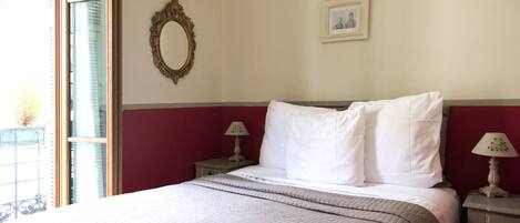 A neatly made bed with a white and brown quilt, a bedside table with a lamp, a mirror on the wall, and a framed picture.