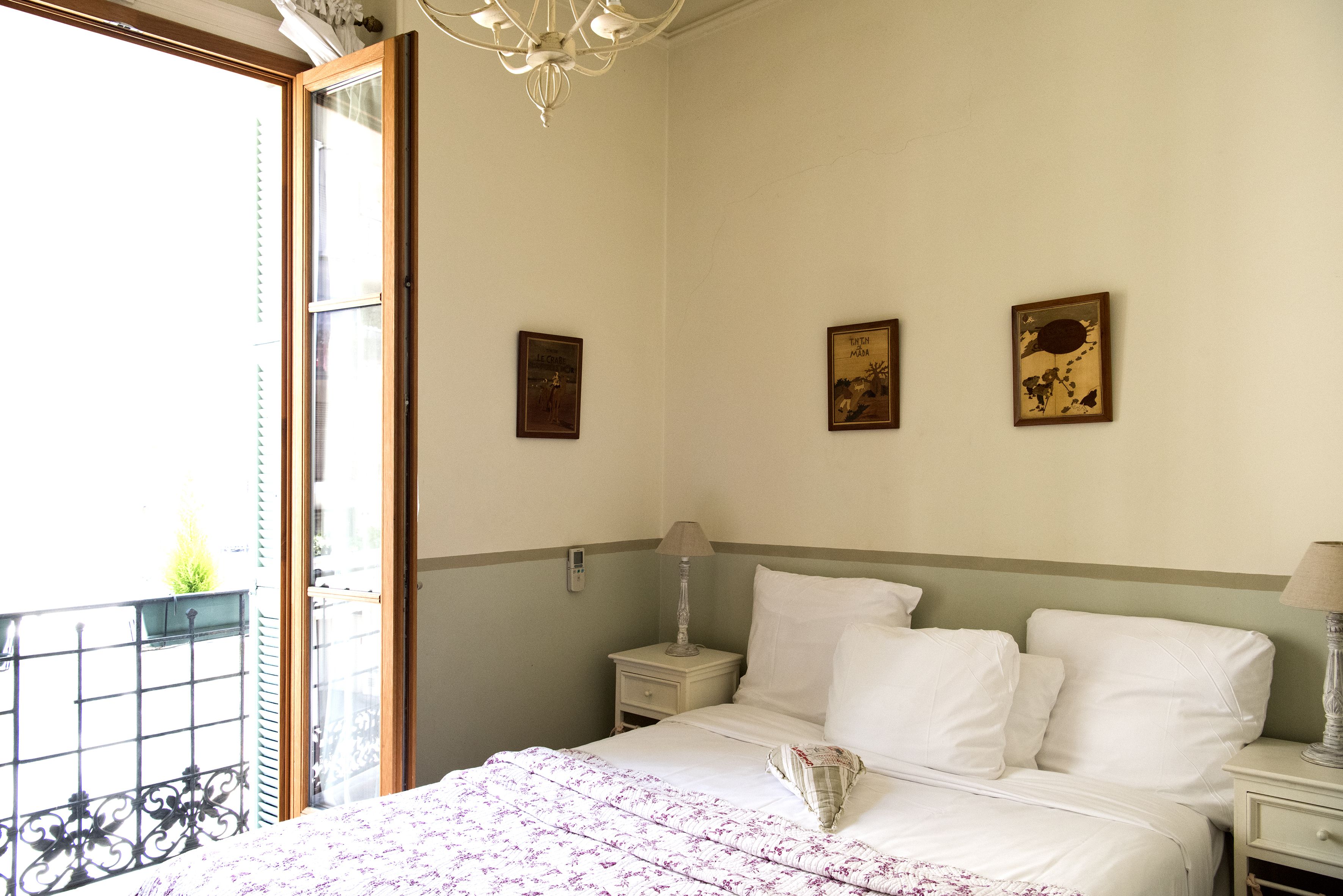 Ein Hotelzimmer mit Bett, Nachttischen, einer Chandelierleuchtre und Kunstwerken an den Wänden.
