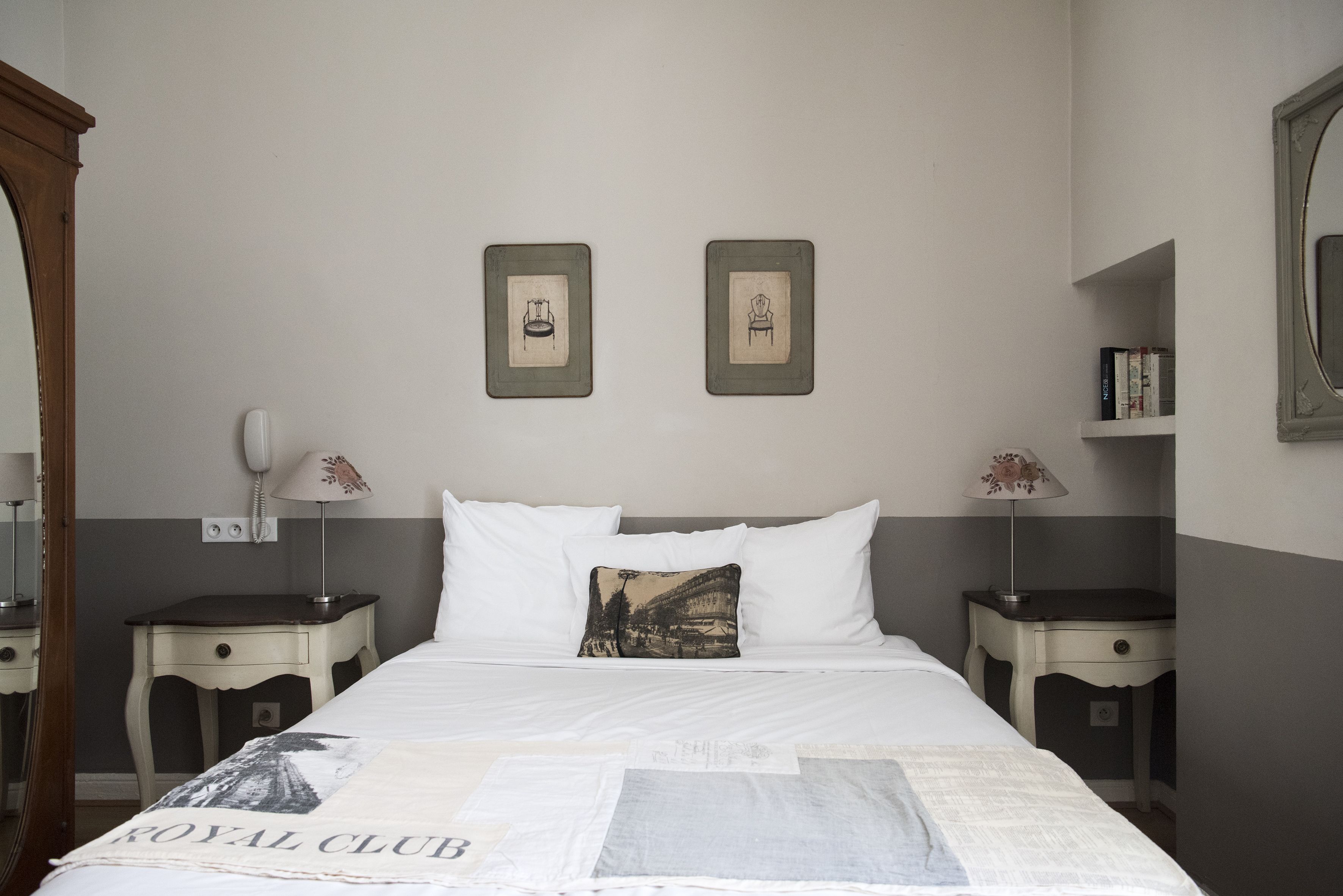 Una cama bien hecha con sábanas blancas, dos mesitas de noche con lámparas y un cuadro en la pared.