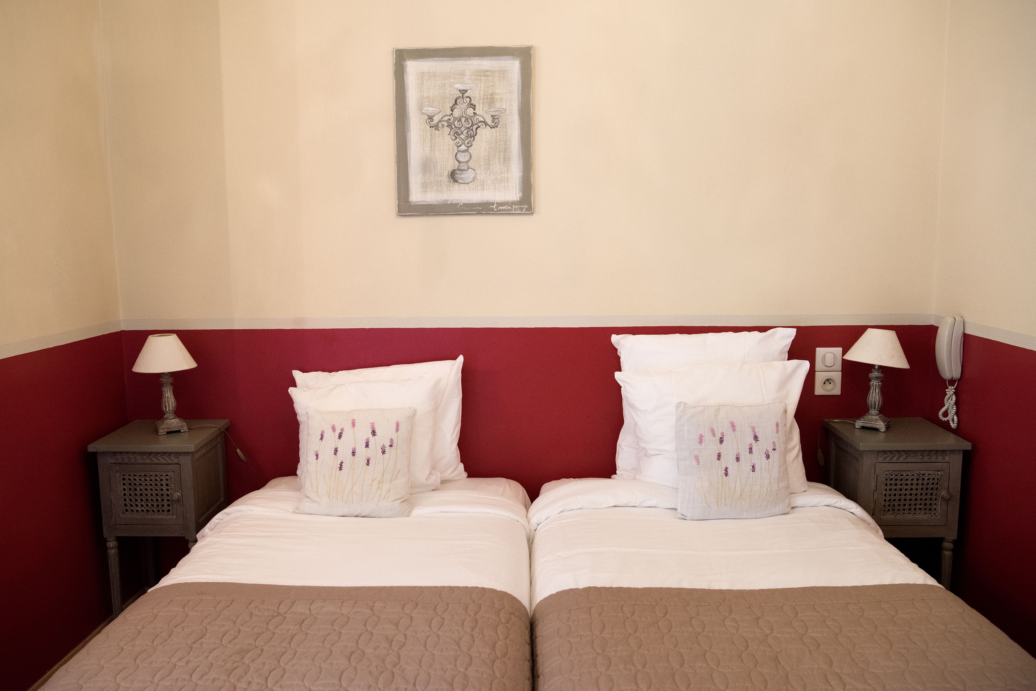 Una cama doble con cabecera roja, dos mesitas de noche con lámparas y una obra de arte enmarcada en la pared.