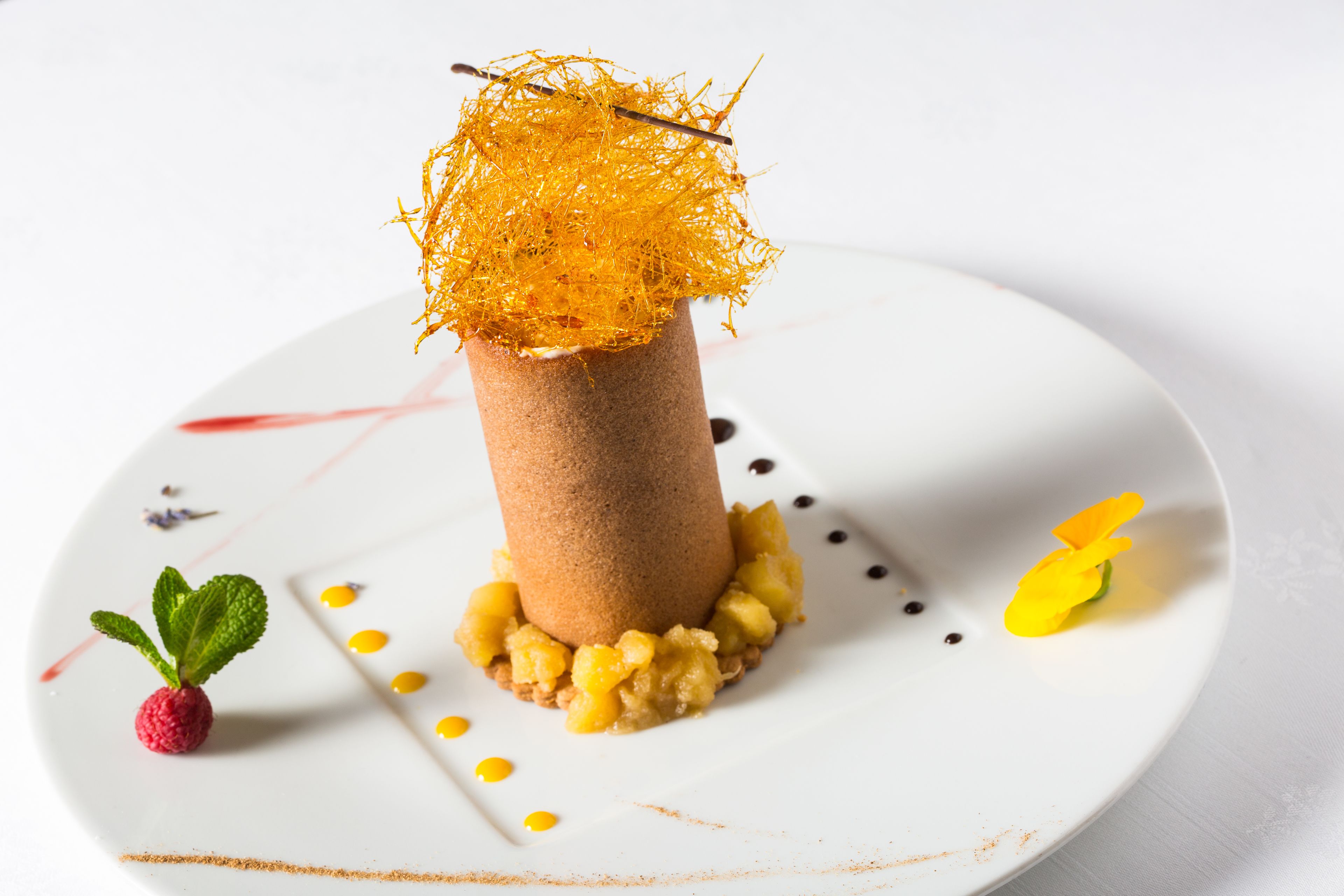 A dessert on a white plate with a raspberry and mint leaf garnish.