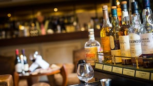 A bar area with various bottles of liquor and a glass on a table. - Les Ursulines (Autun)