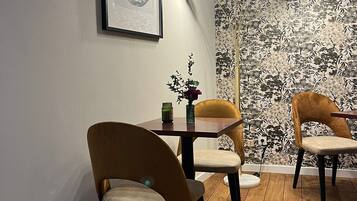 Un coin repas avec une table ronde, deux chaises, une œuvre d’art encadrée, une lampe sur pied et un papier peint à motifs floraux.