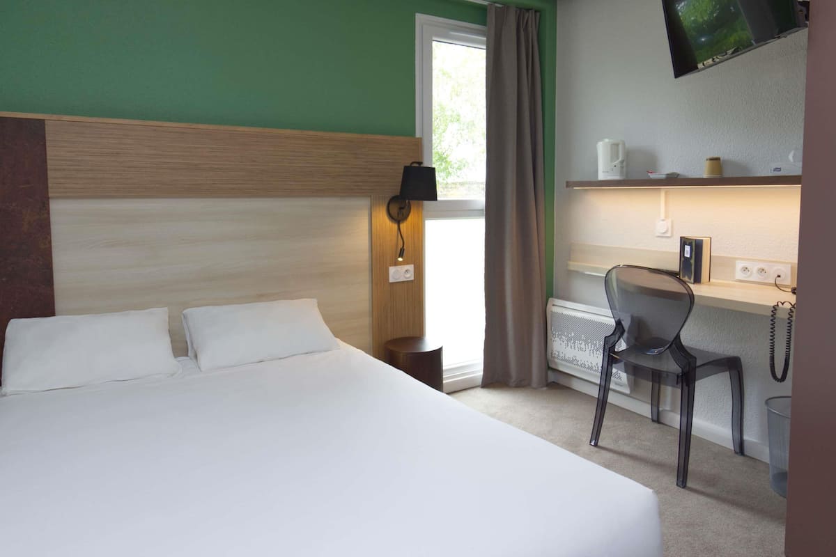 A hotel room with a bed, a desk, a chair, a television, and a window with curtains.