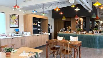 Un restaurant moderne avec des meubles en bois, un coin bar et des lampes suspendues aux couleurs vives.