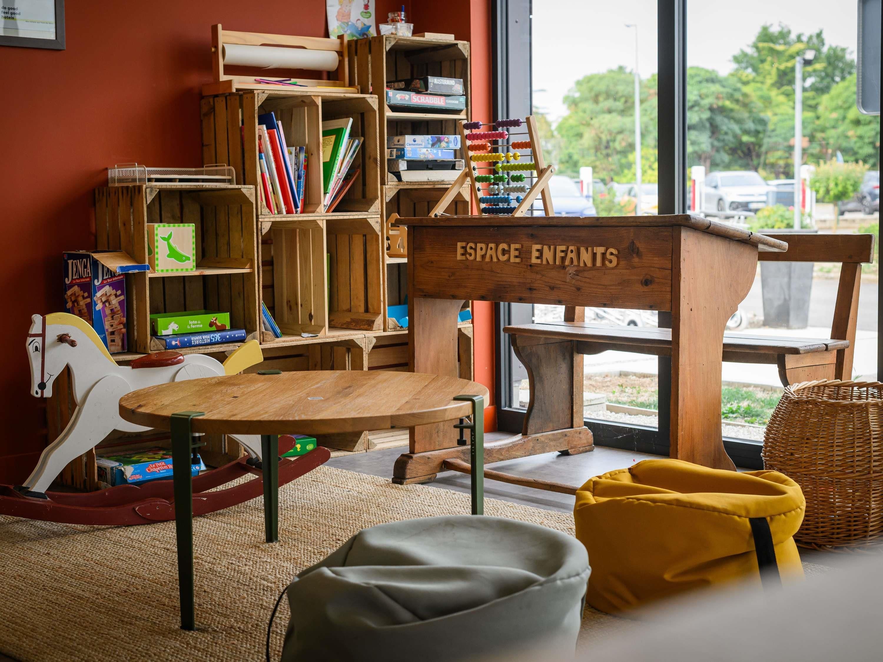 Un espace de jeux pour enfants avec des meubles en bois, une table et une bibliothèque remplie de livres et de jouets.