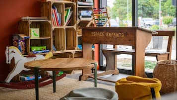Un espace de jeux pour enfants avec des meubles en bois, une table et une bibliothèque remplie de livres et de jouets.