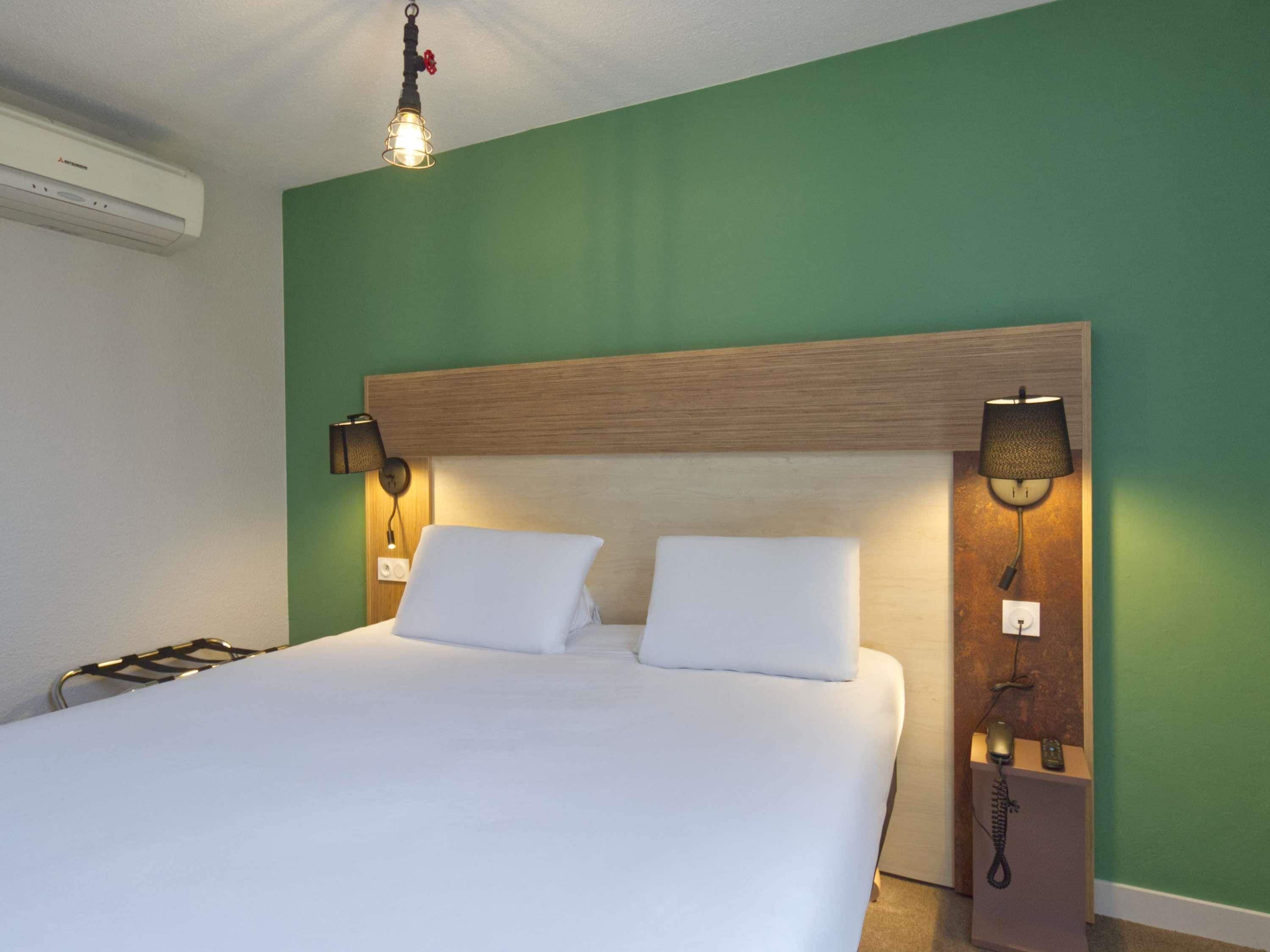 Una habitación de hotel con una cama grande, dos lámparas de noche, un teléfono y aire acondicionado instalado en la pared.