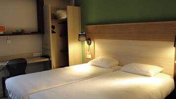 Una cama doble con ropa de cama blanca, un escritorio con una silla, un armario y una lámpara en la pared.