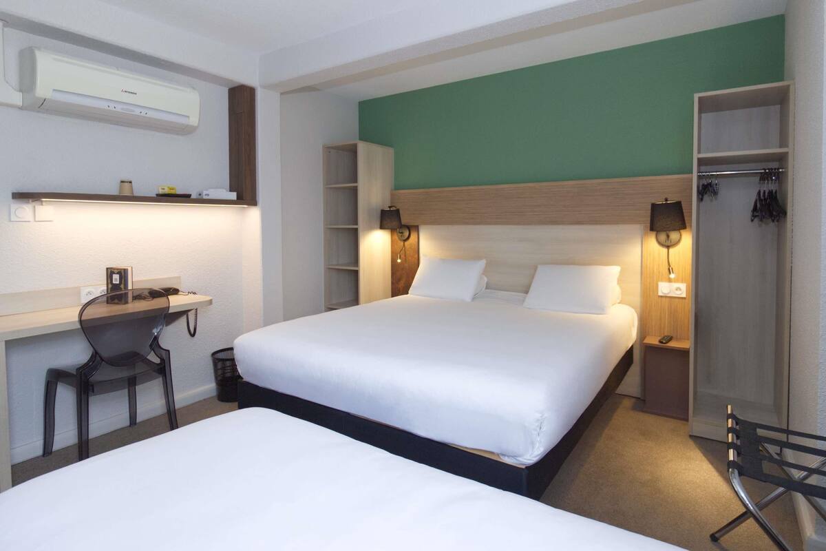 A hotel room with a bed, a desk, a chair, a wardrobe, and a mirror.