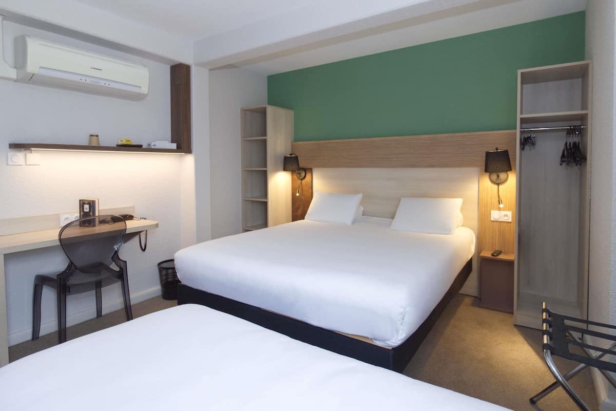 A hotel room with a bed, a desk, a chair, a wardrobe, and a mirror.