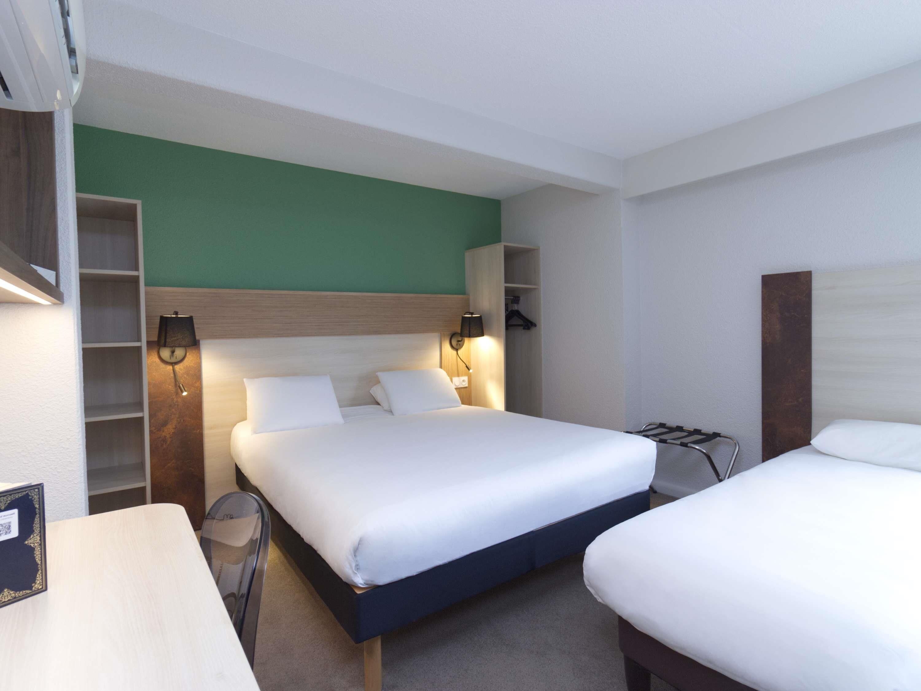 A hotel room with a bed, bedside tables, a desk, and a wardrobe.