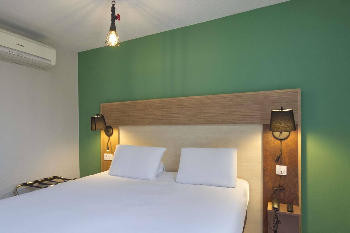 A hotel room with a large bed, two bedside lamps, a telephone, and a wall-mounted air conditioner.