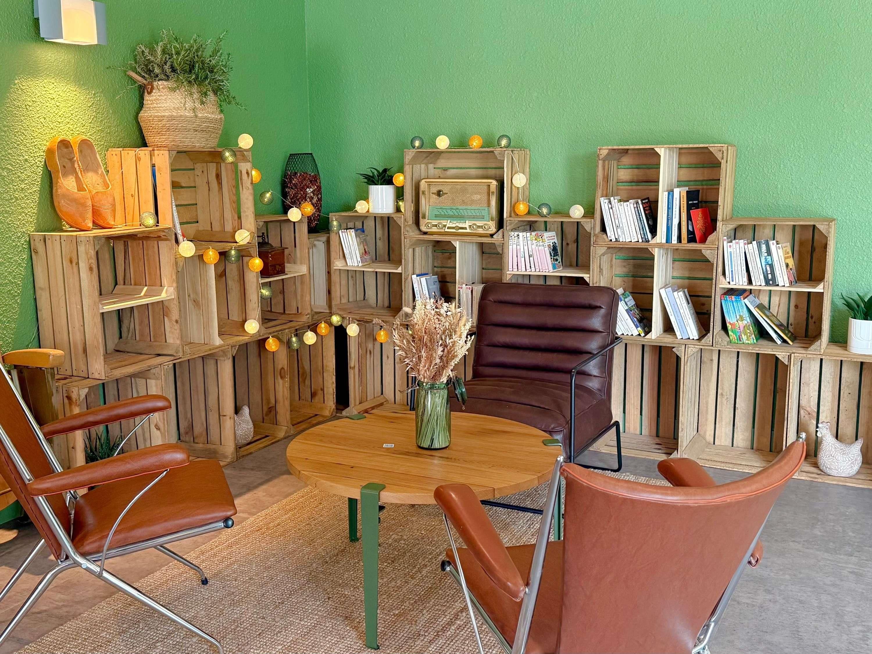 Una habitación con una mesa redonda de madera, dos sillas de cuero marrón y estantes de madera con libros y objetos decorativos.