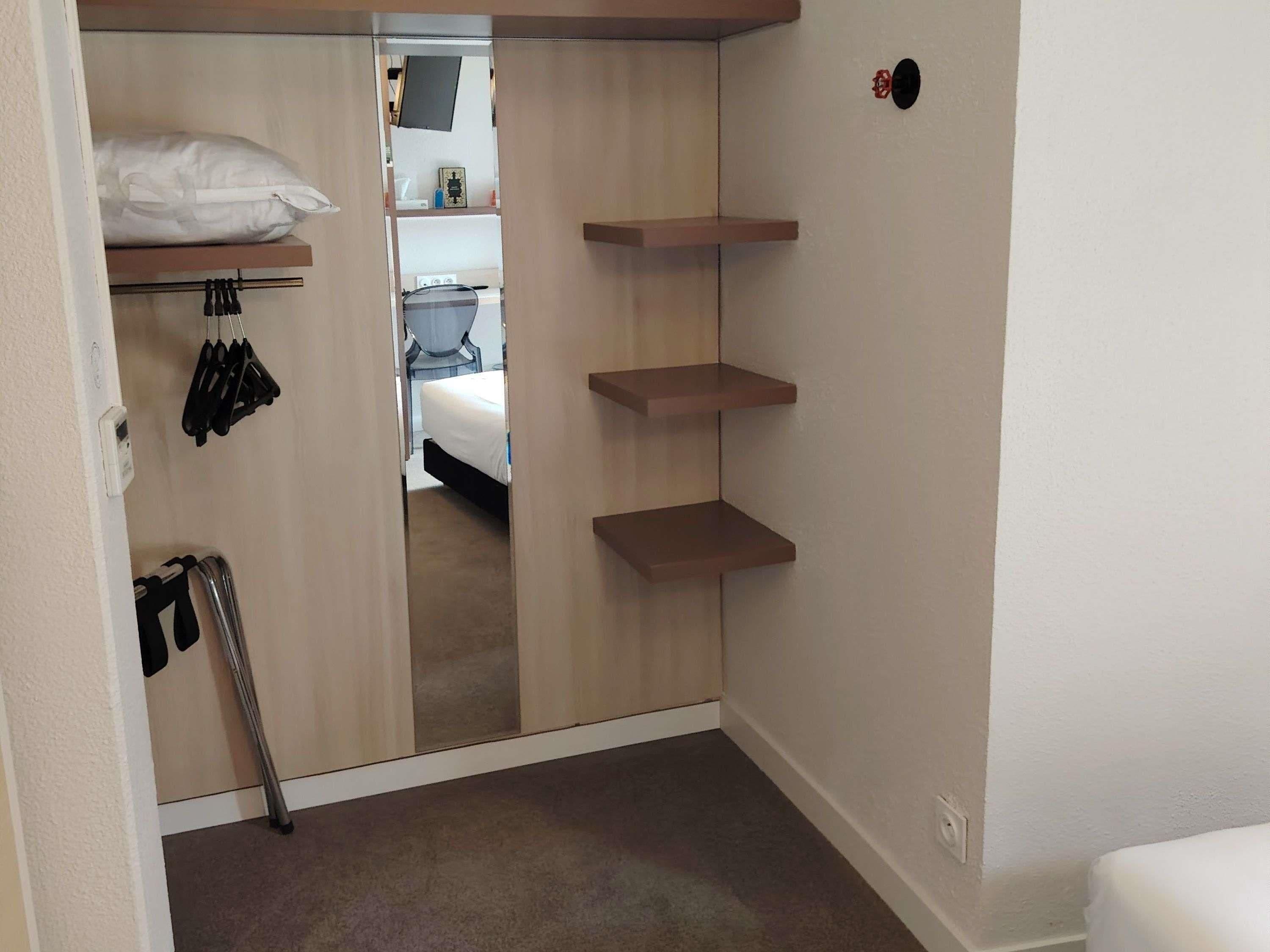 Ein Zimmer mit einem Bett, einem Kleiderschrank mit darin befindlichen Kleidungsstücken und einem Schuhregal.