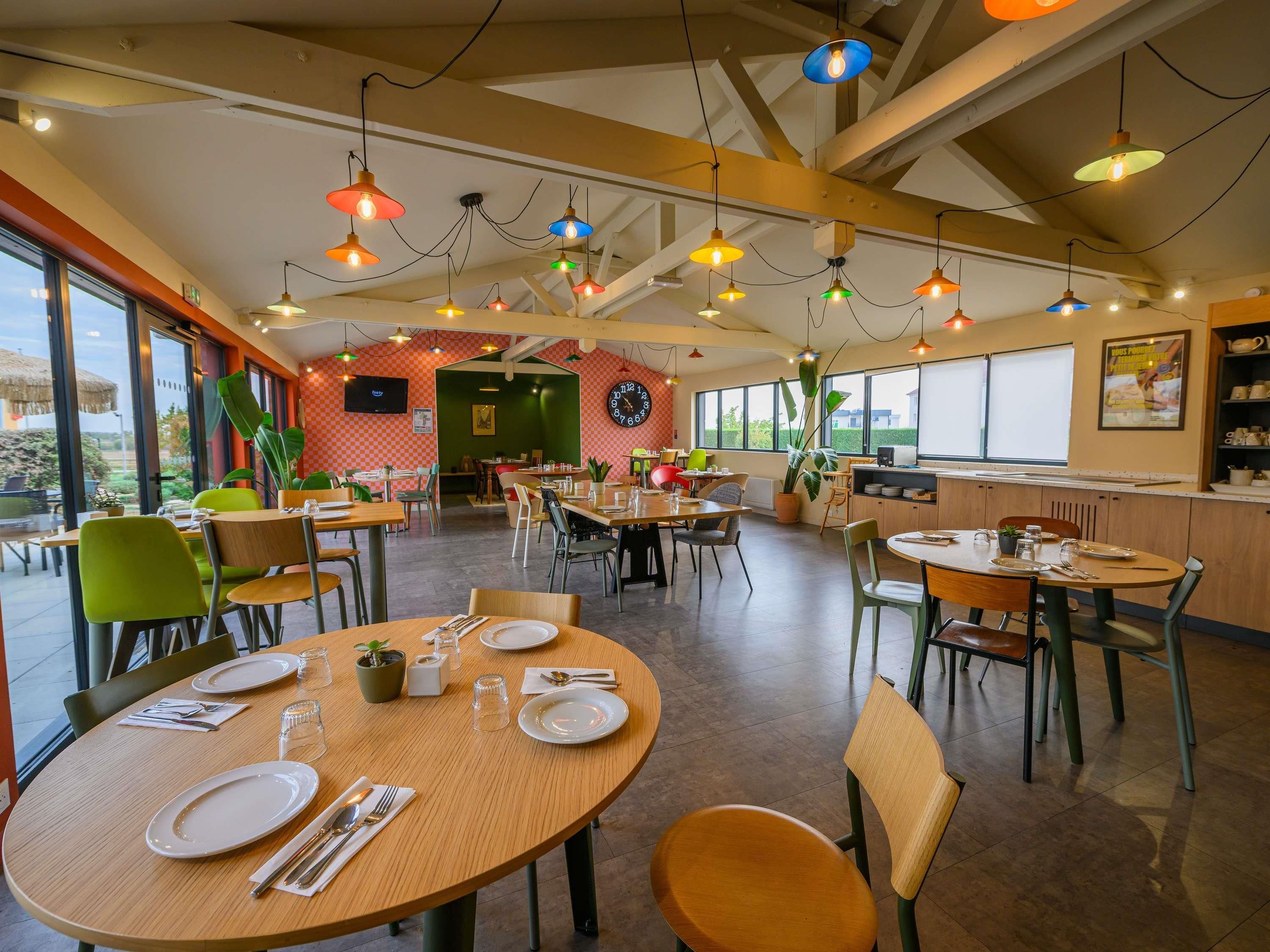 Ein Restaurant mit mehreren Tischen, Stühlen, einer Küchenzeile und großen Fenstern.