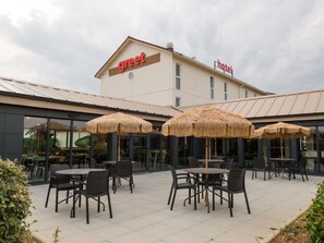 A hotel named 'Greet' with outdoor seating and thatched umbrellas. - greet Hotel Dijon Sud Longvic (Longvic)