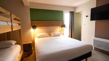 Ein Hotelzimmer mit Etagenbett, einem Einzelbett, einem wandmontierten Fernseher und einem Nachttisch.