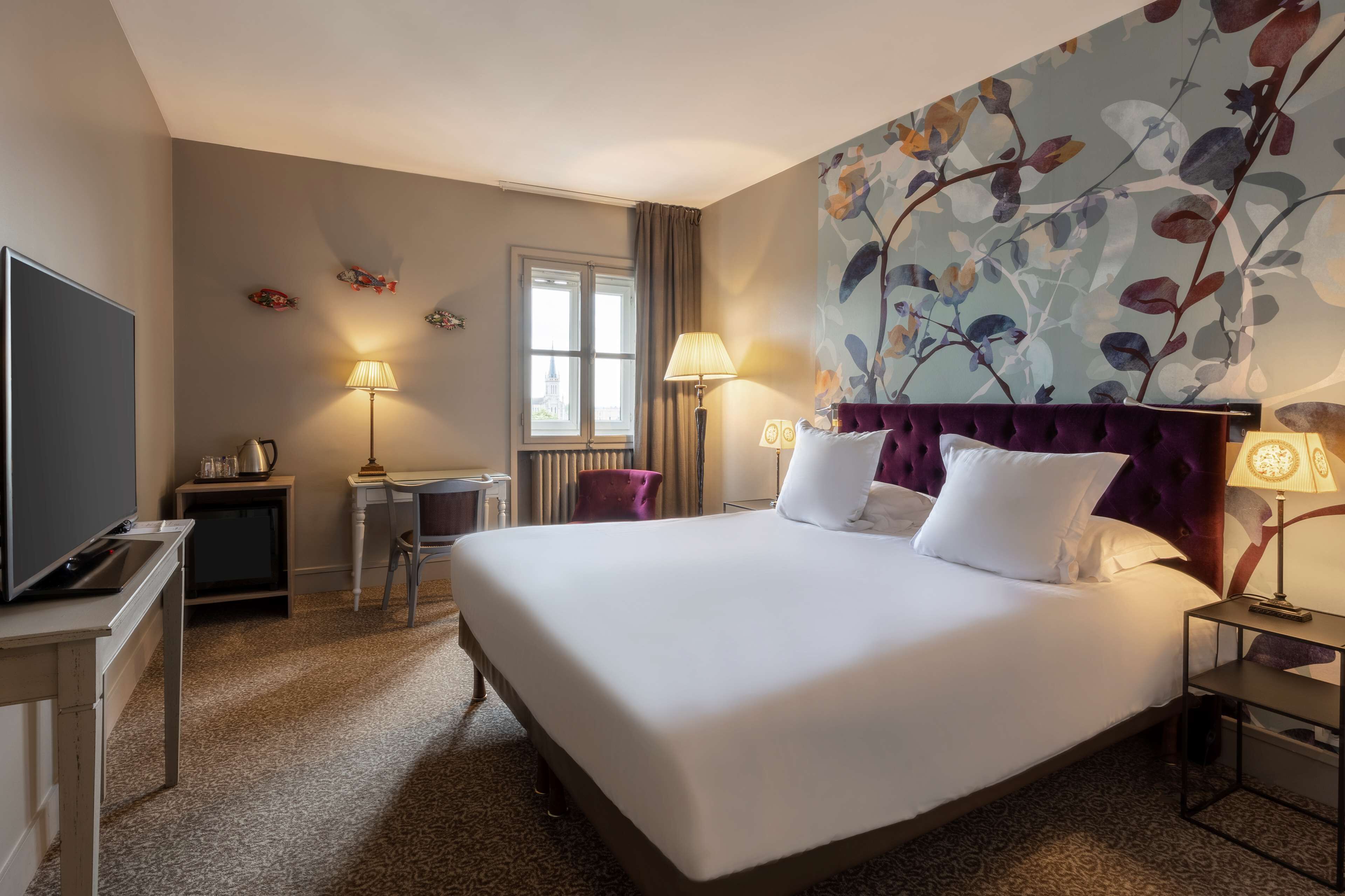 A hotel room with a large bed, a desk with a chair, a television, and a window with curtains.