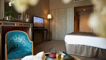 A hotel room with a bed, a TV, a chair, and a tray with a book, teapot, and cup.