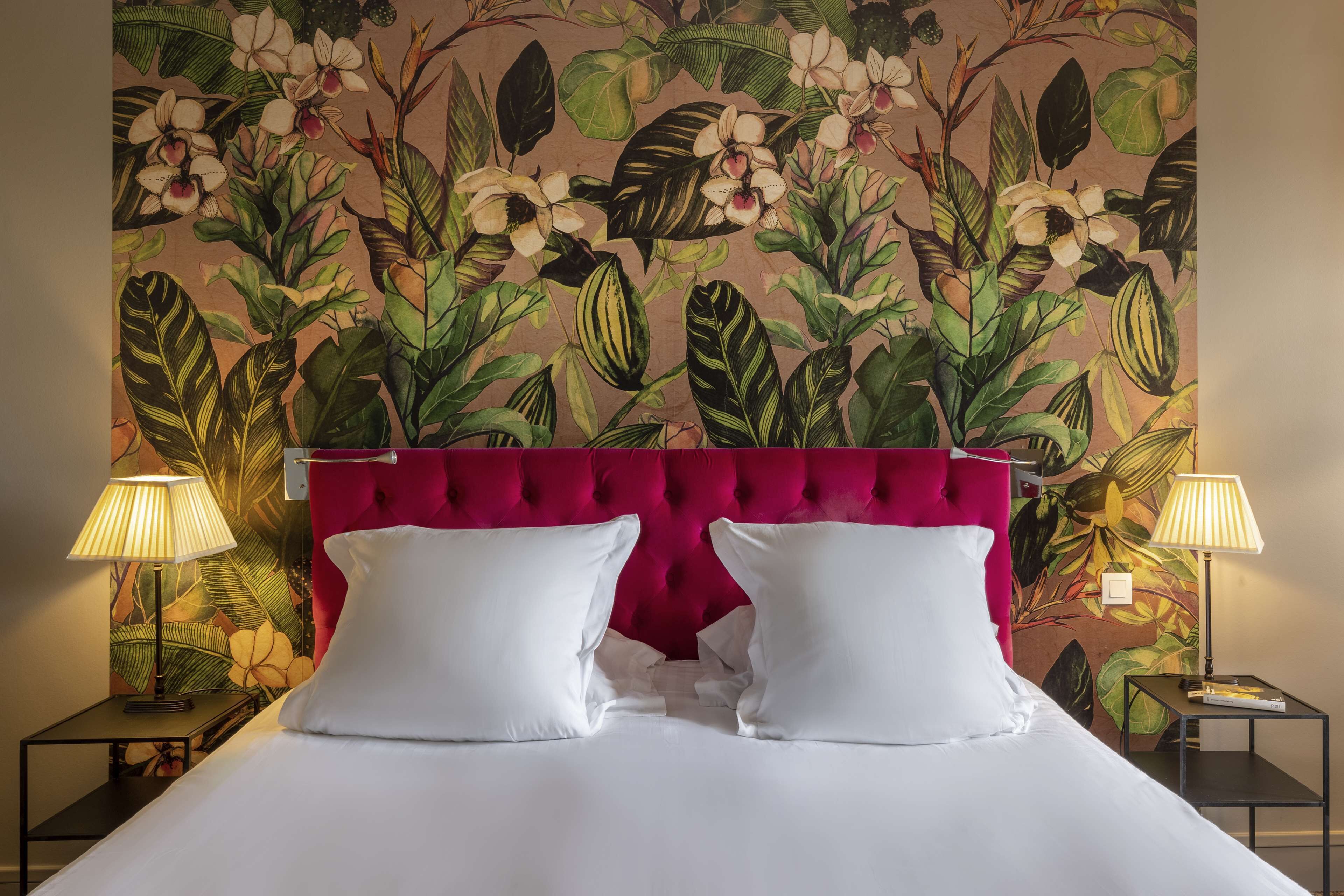 Een hotelkamer met een bed, twee bedlampen, een rode hoofdbord en bloemenbehang.