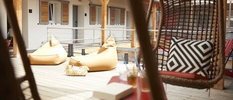 A wooden deck with outdoor seating, including bean bags and a wicker chair with a patterned cushion.