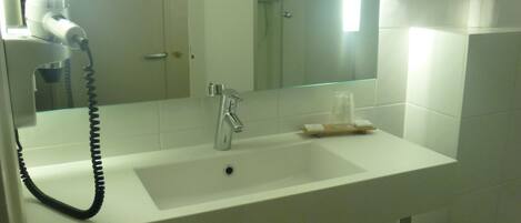 Un baño con un lavabo blanco, un espejo, un secador de pelo de mano y dos toallas colgadas en un perchero.